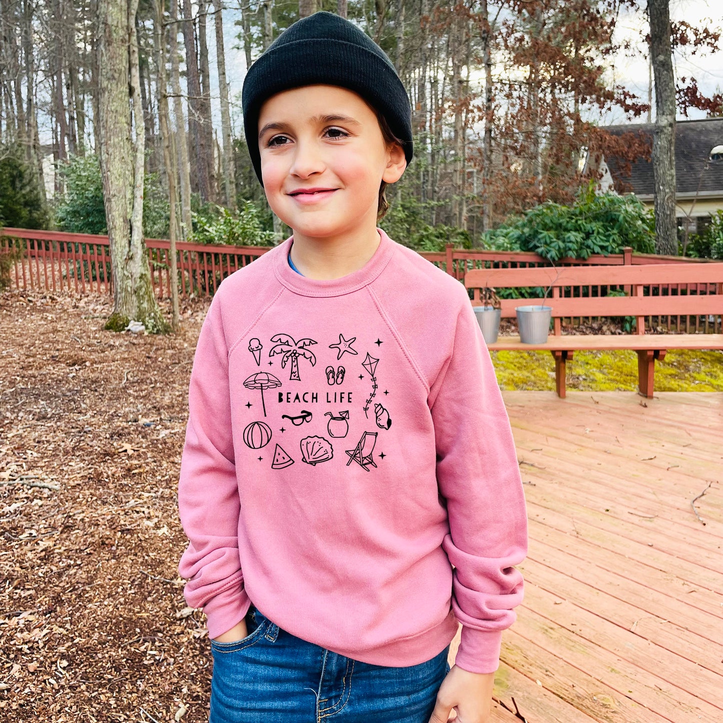 a young boy standing on a deck wearing a pink sweatshirt