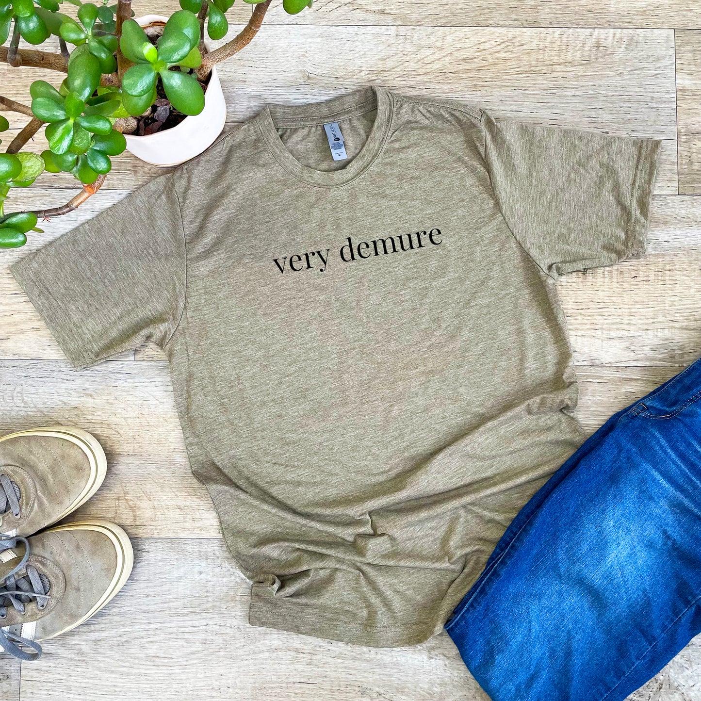 a t - shirt that says very demure next to a potted plant