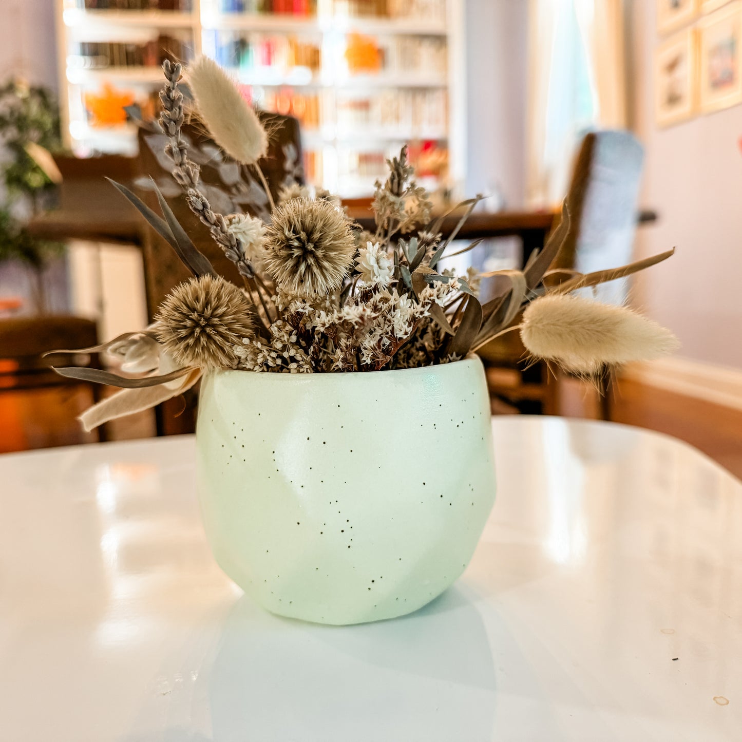 a white vase filled with dried flowers on top of a table