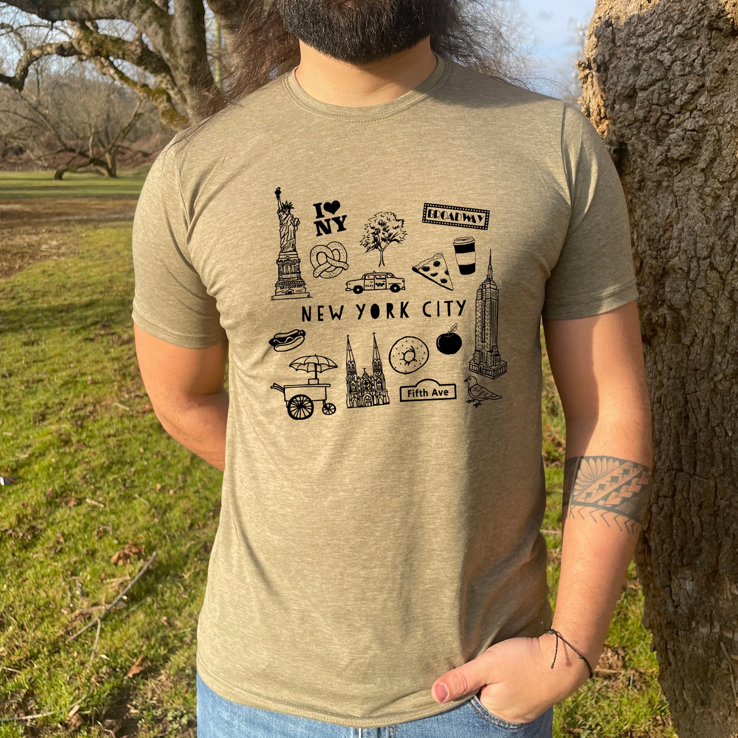 a man standing next to a tree wearing a new york city t - shirt