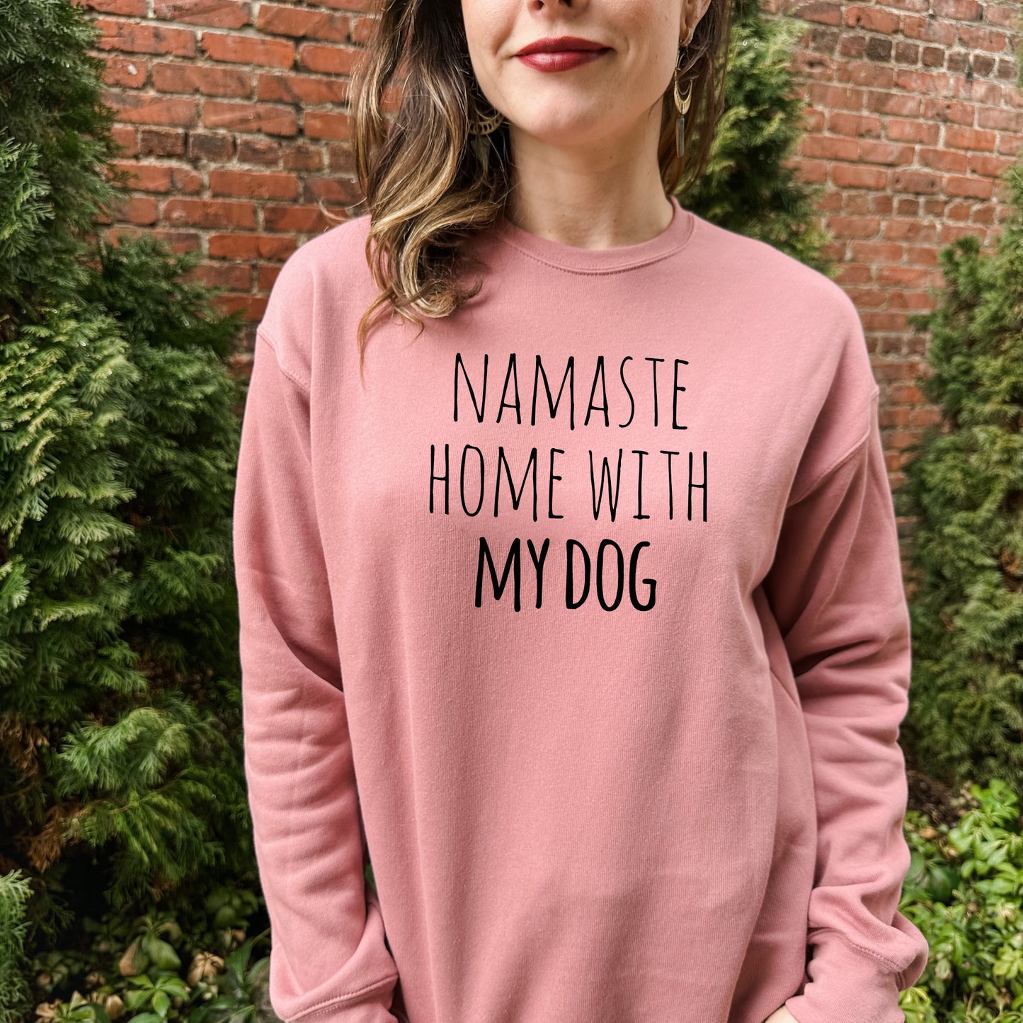 a woman wearing a pink sweatshirt that says namaste home with my dog