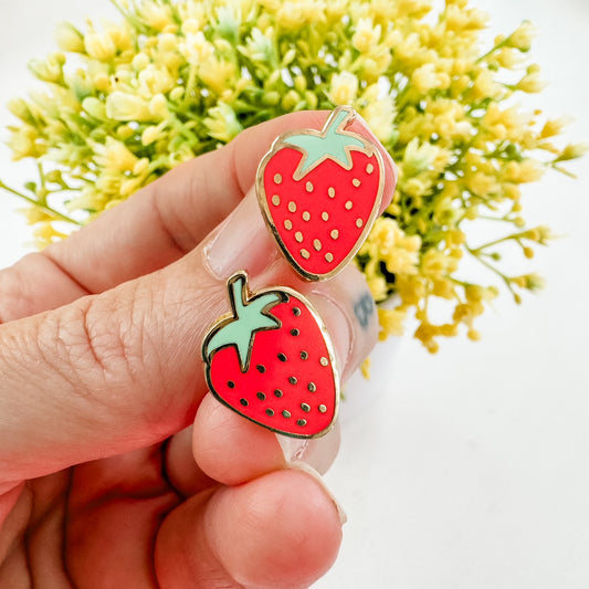 a hand holding a pair of earrings with a strawberry on it