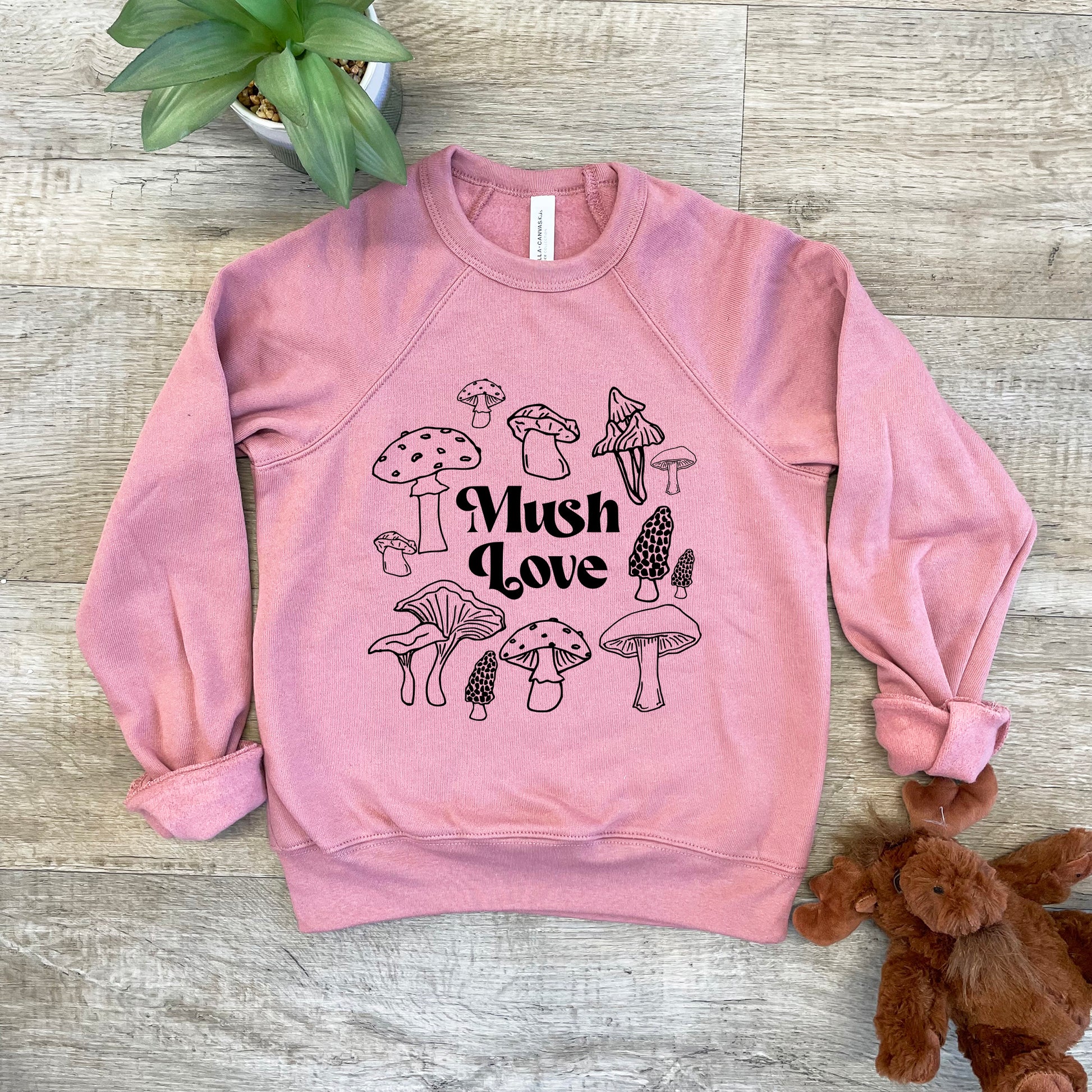 a pink sweatshirt with mushrooms on it next to a teddy bear