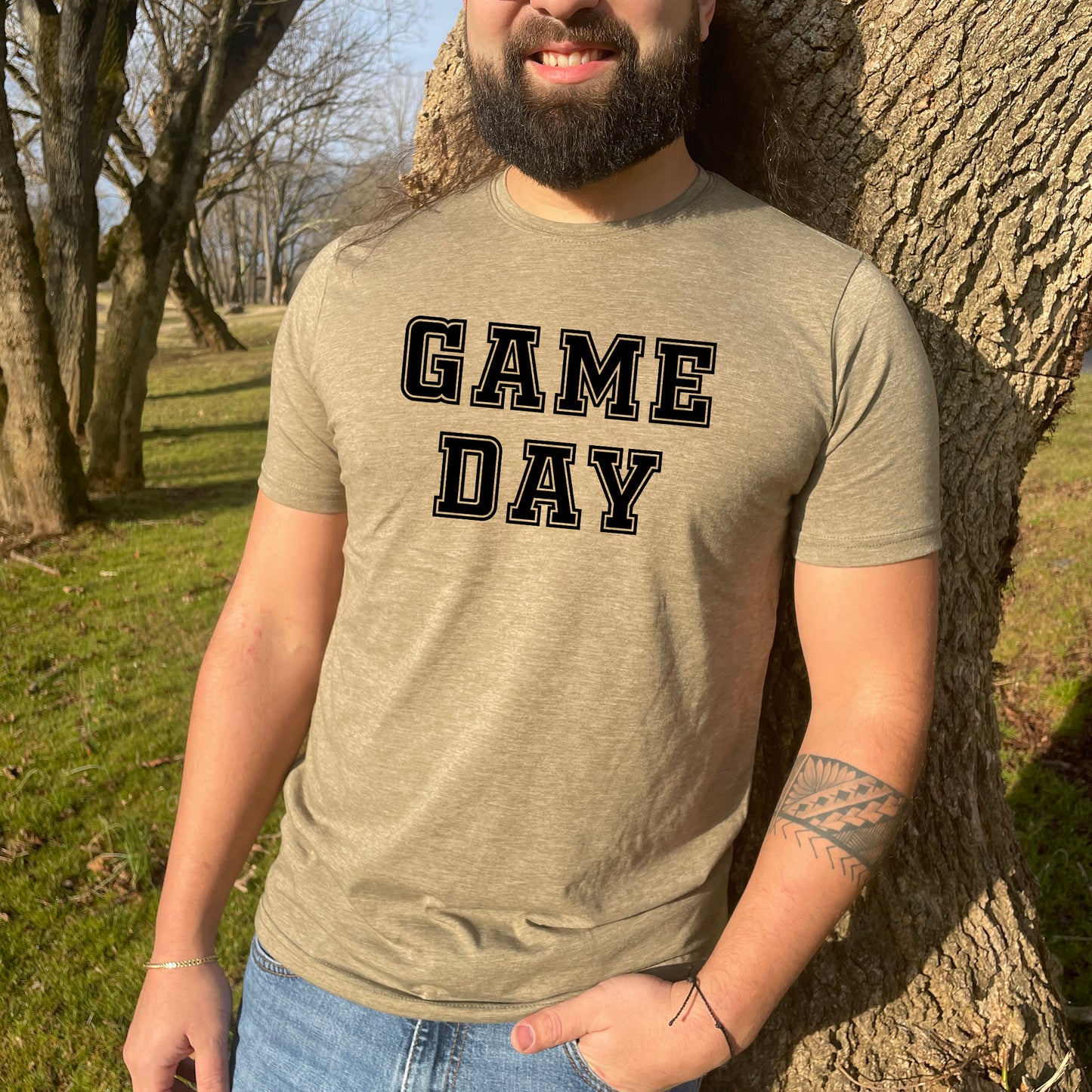 a man standing next to a tree wearing a game day shirt