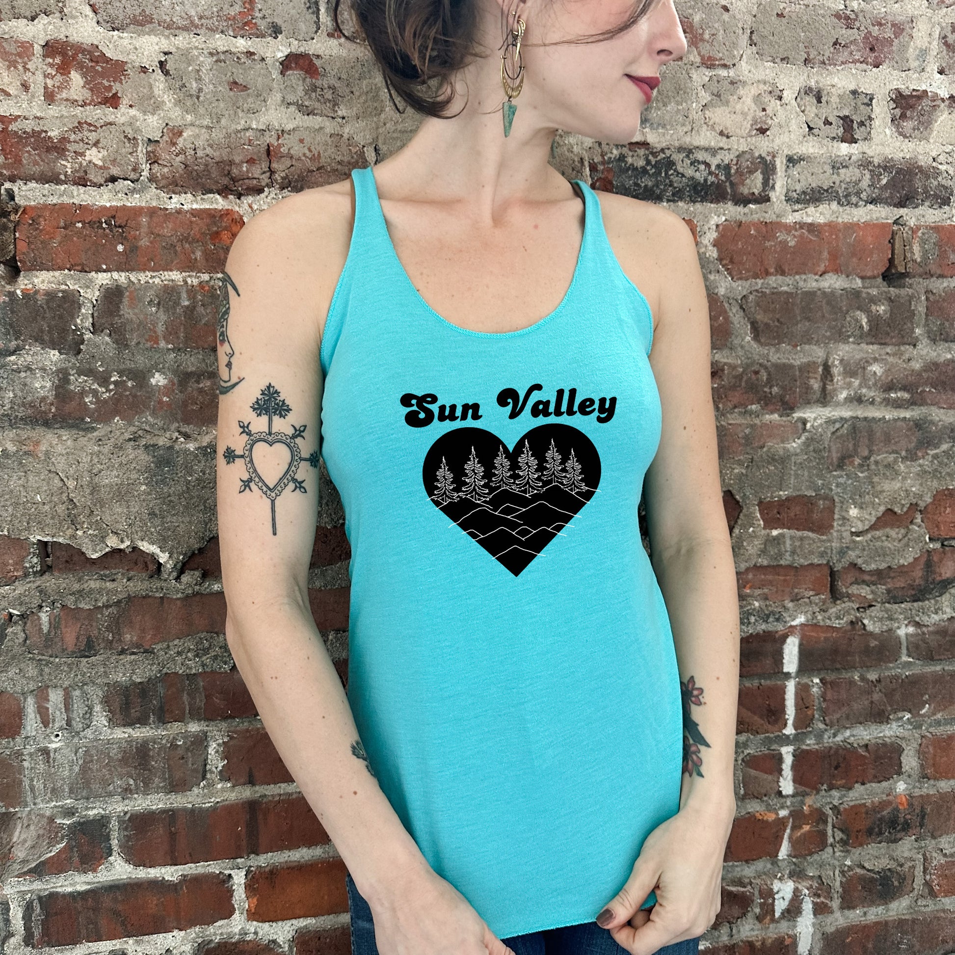 a woman wearing a sun valley tank top standing in front of a brick wall