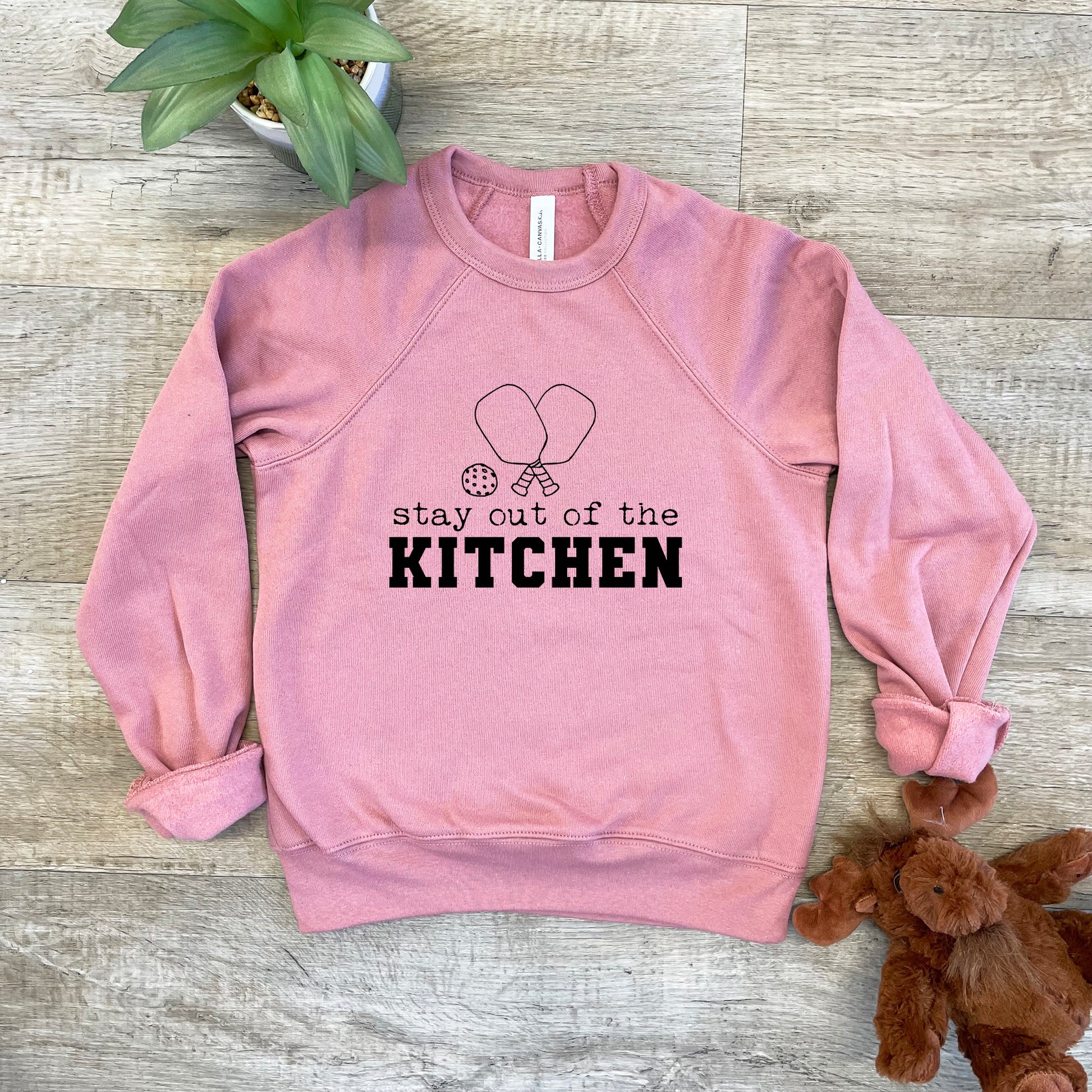 a pink sweatshirt that says stay out of the kitchen next to a teddy bear
