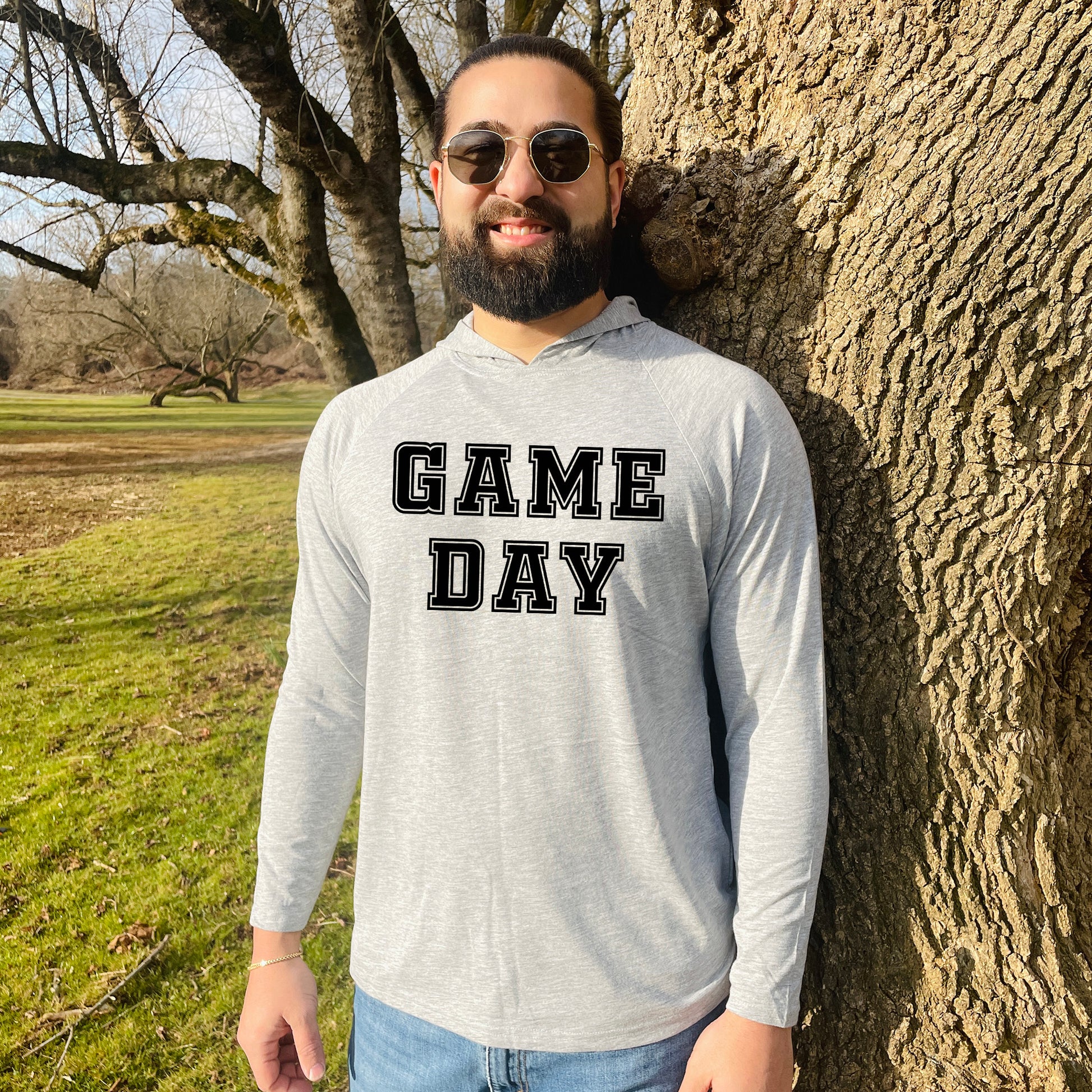 a man standing next to a tree with a game day shirt on