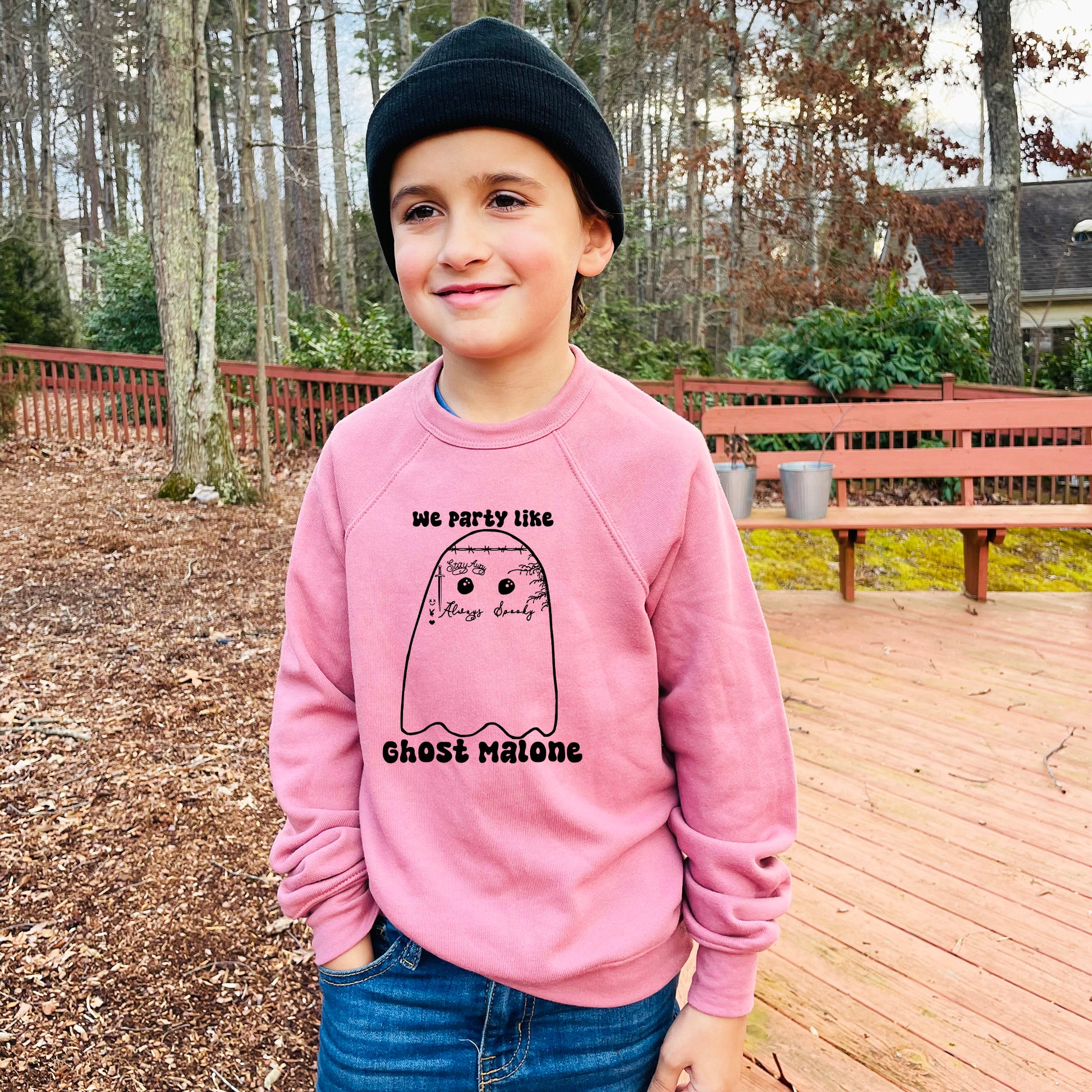 a young boy standing on a deck wearing a pink sweatshirt