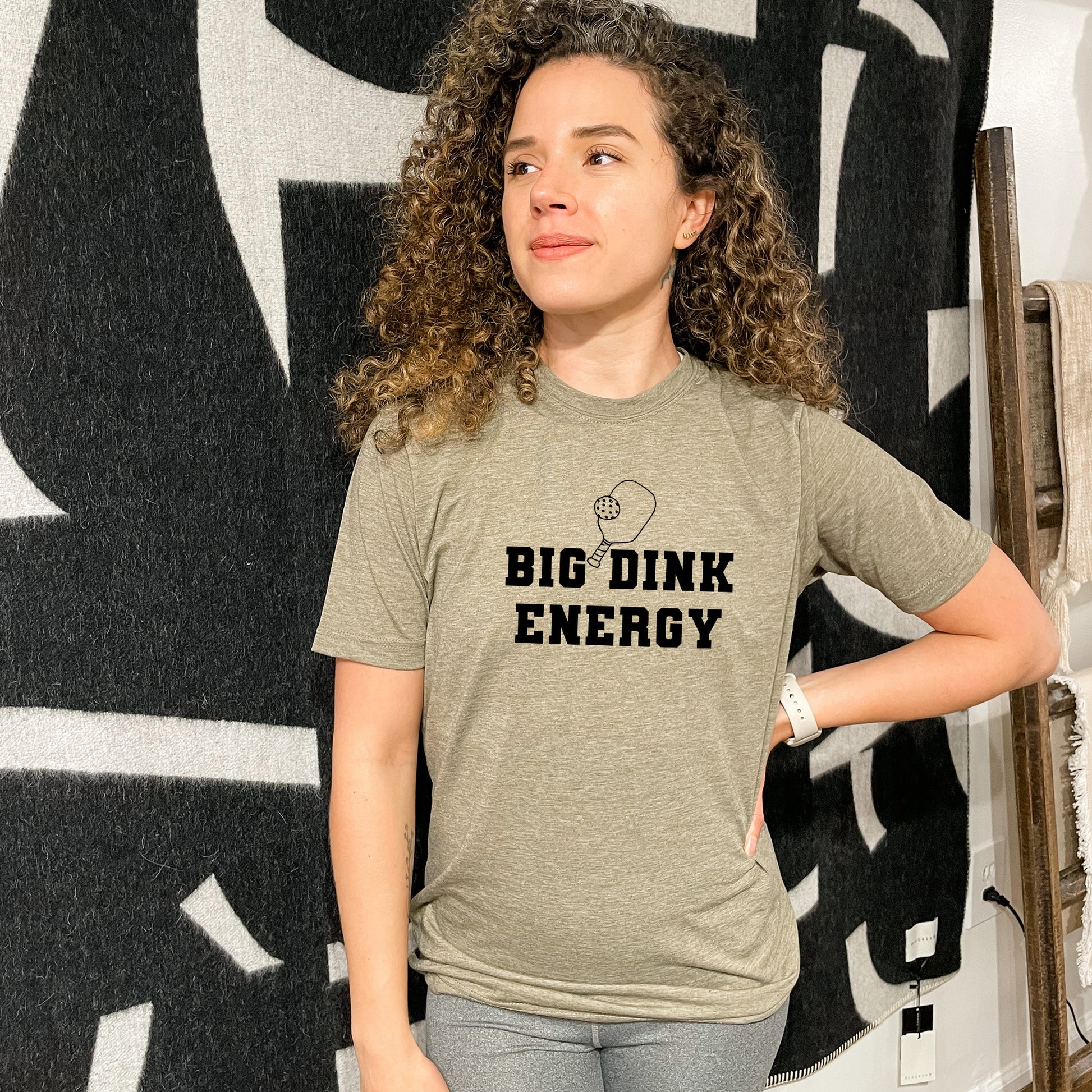 a woman standing in front of a wall with a big drink energy t - shirt