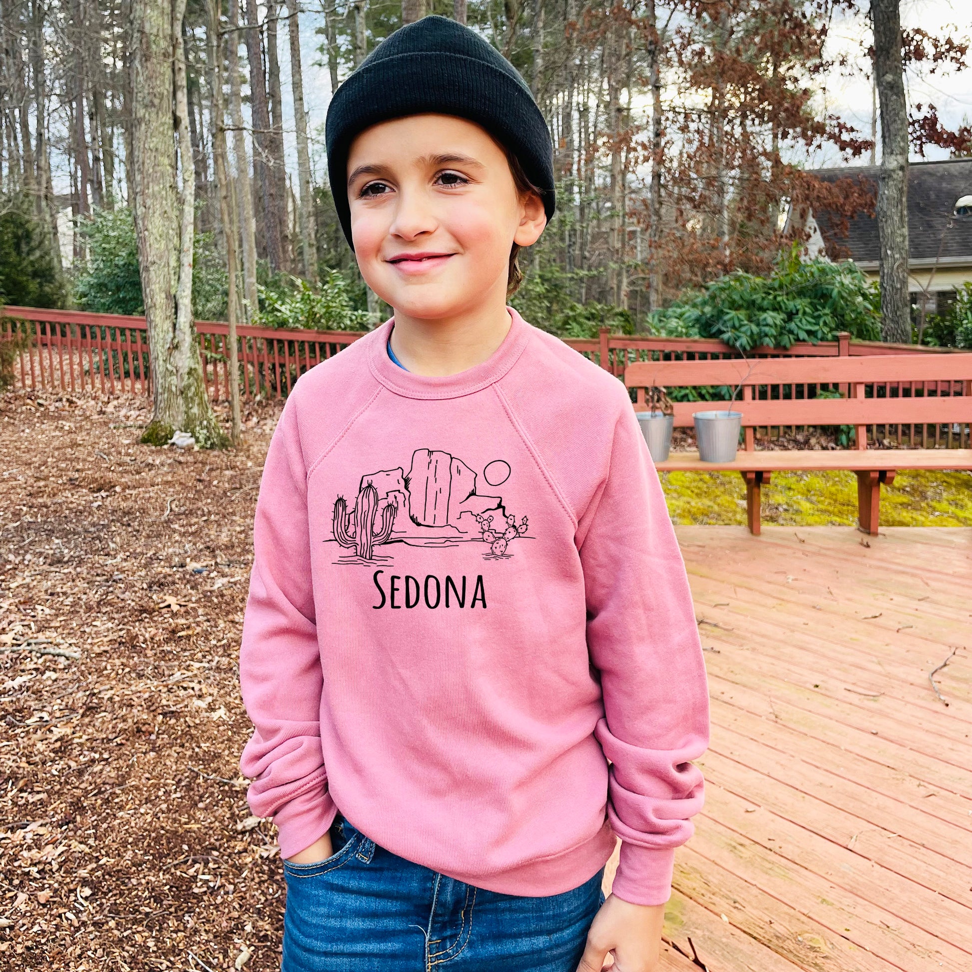 a young boy standing on a deck wearing a pink sweatshirt