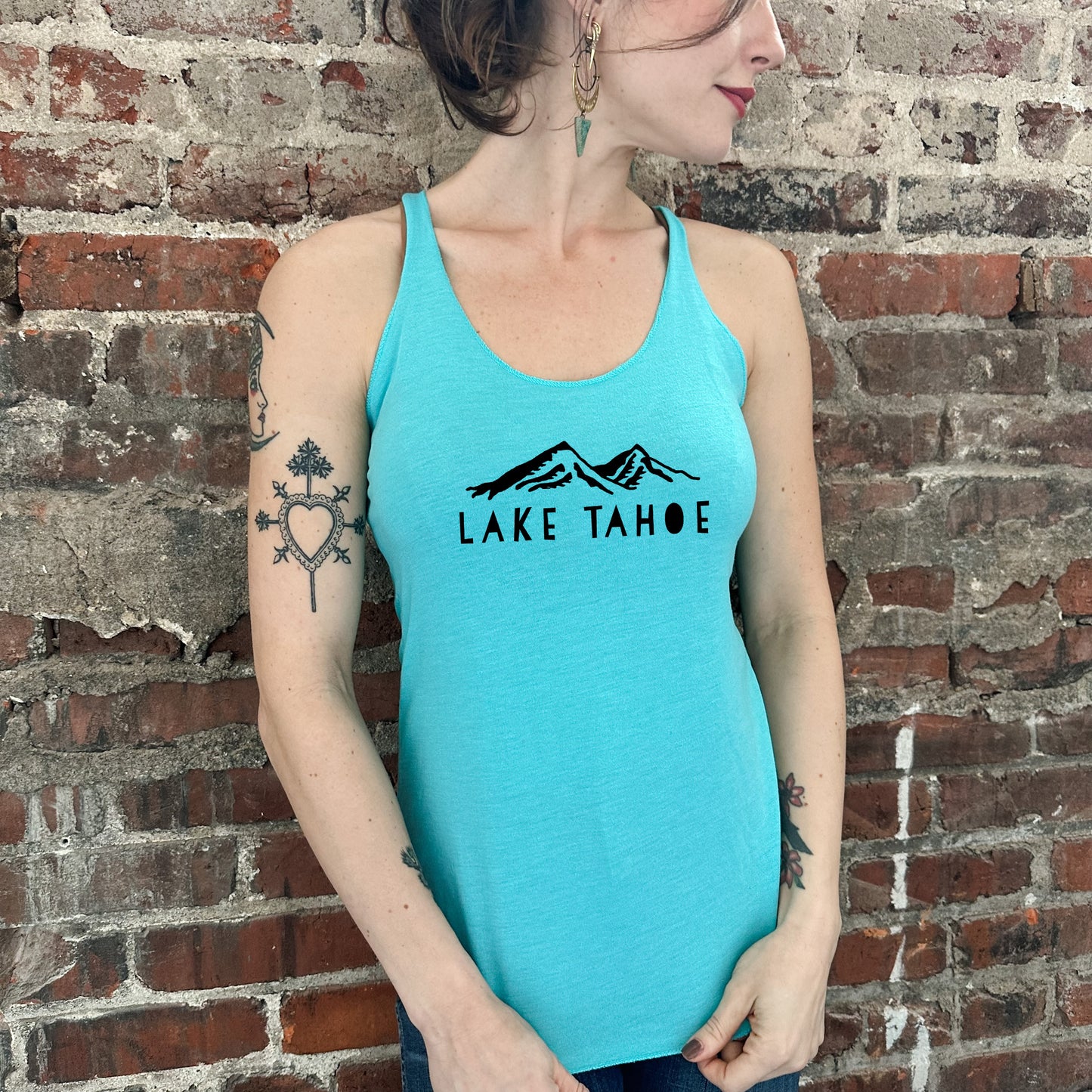 a woman wearing a lake tahoe tank top standing in front of a brick wall