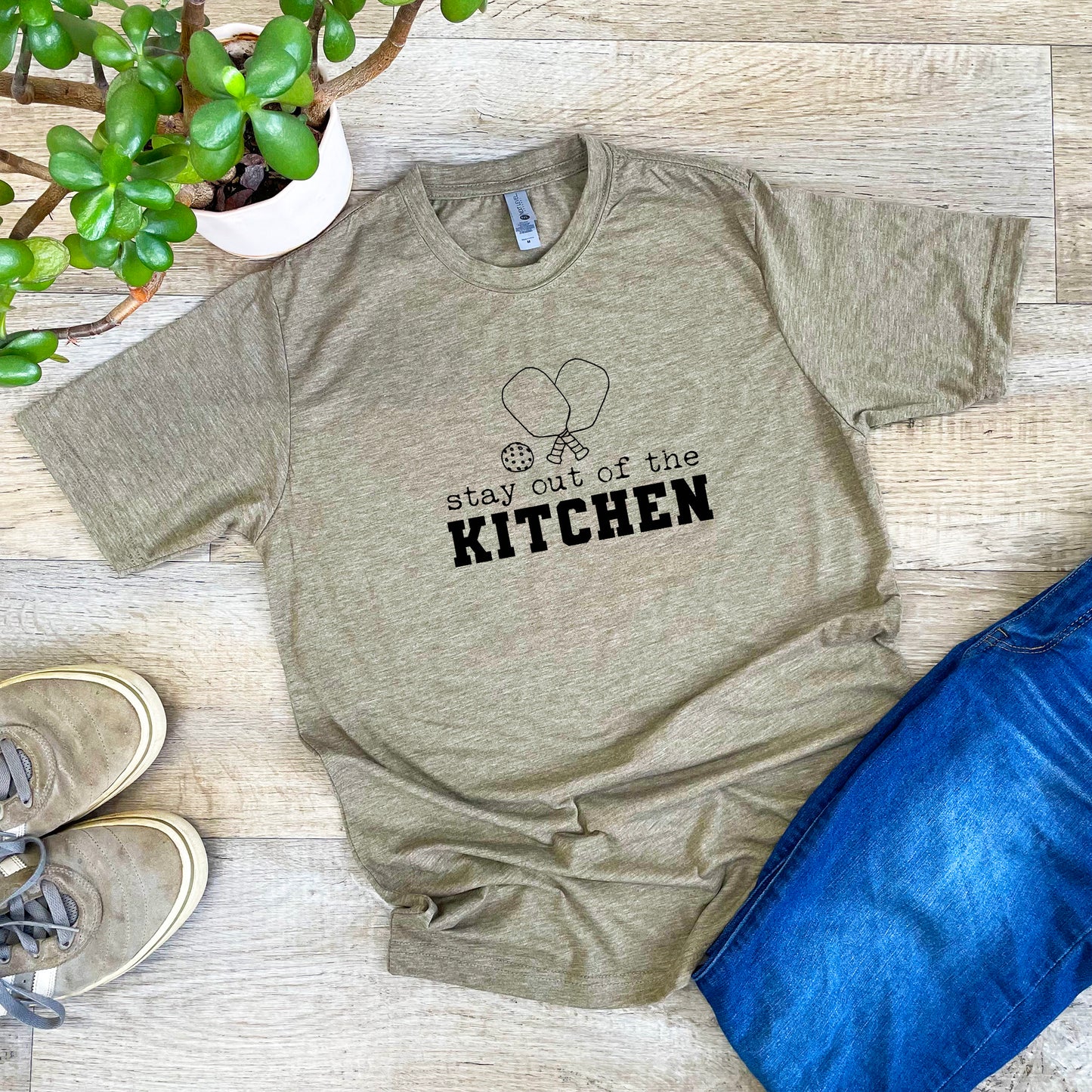 a t - shirt that says stay out of the kitchen next to a potted