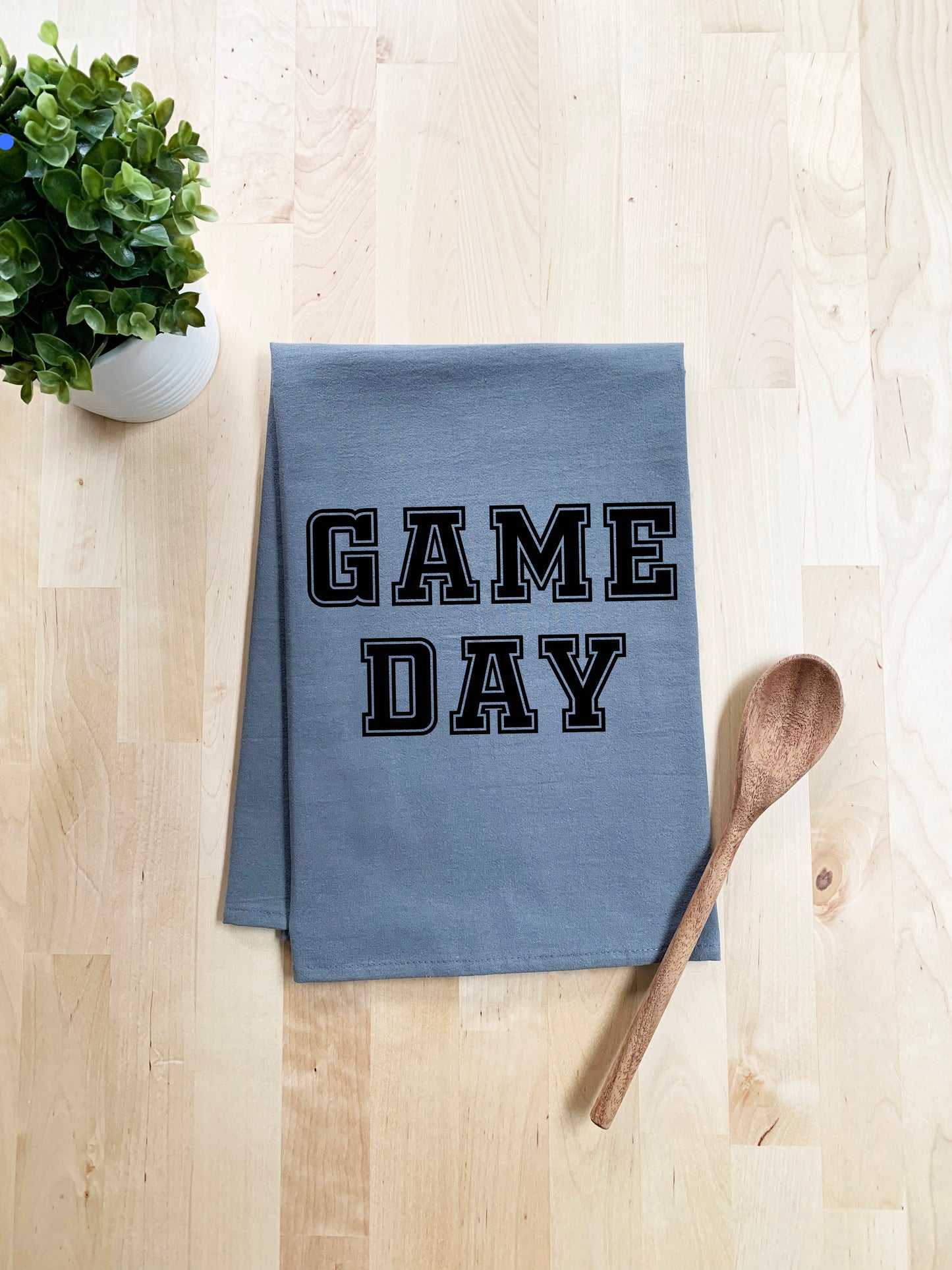 a blue dish towel with the words game day on it next to a wooden spoon