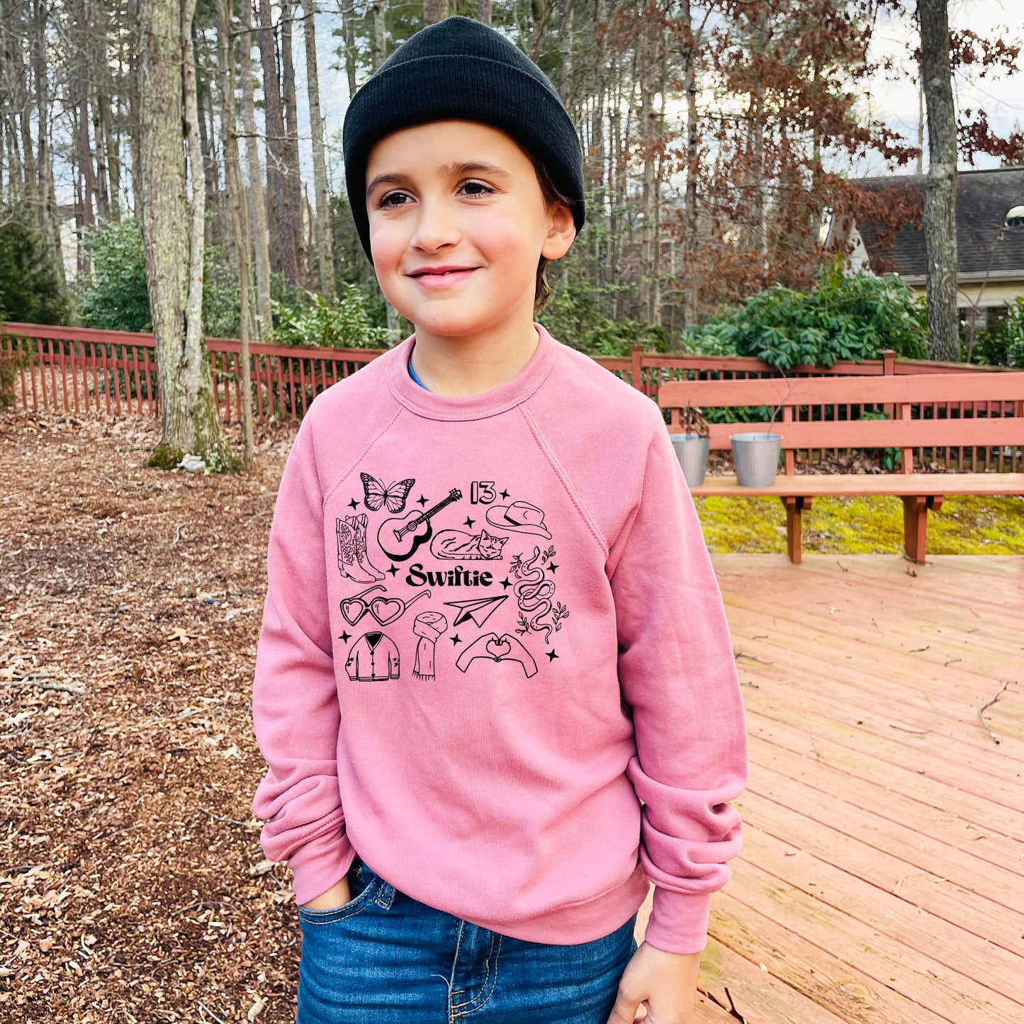 a young boy standing on a deck wearing a pink sweater