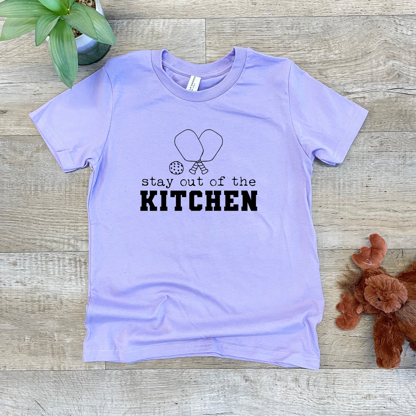 a t - shirt that says stay out of the kitchen next to a teddy bear