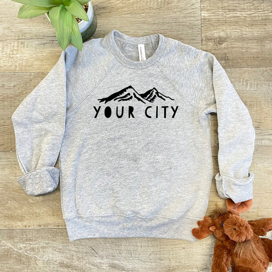 a grey sweatshirt with the words your city on it next to a teddy bear