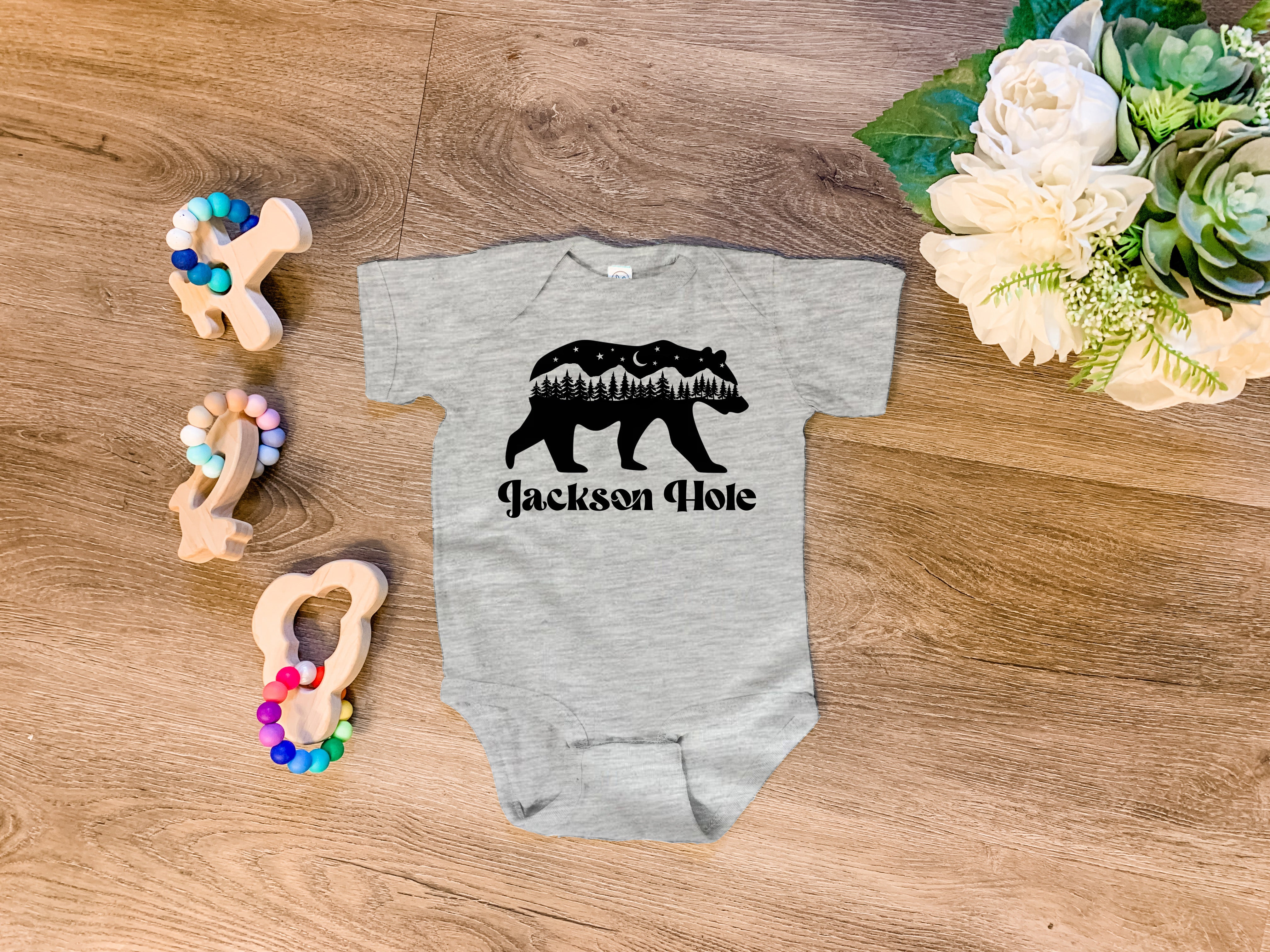 a baby bodysuit with a bear and trees on it