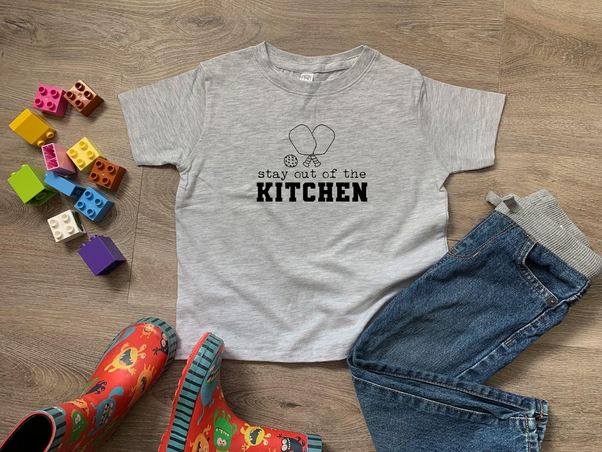 a t - shirt that says stay out of the kitchen next to a pair of