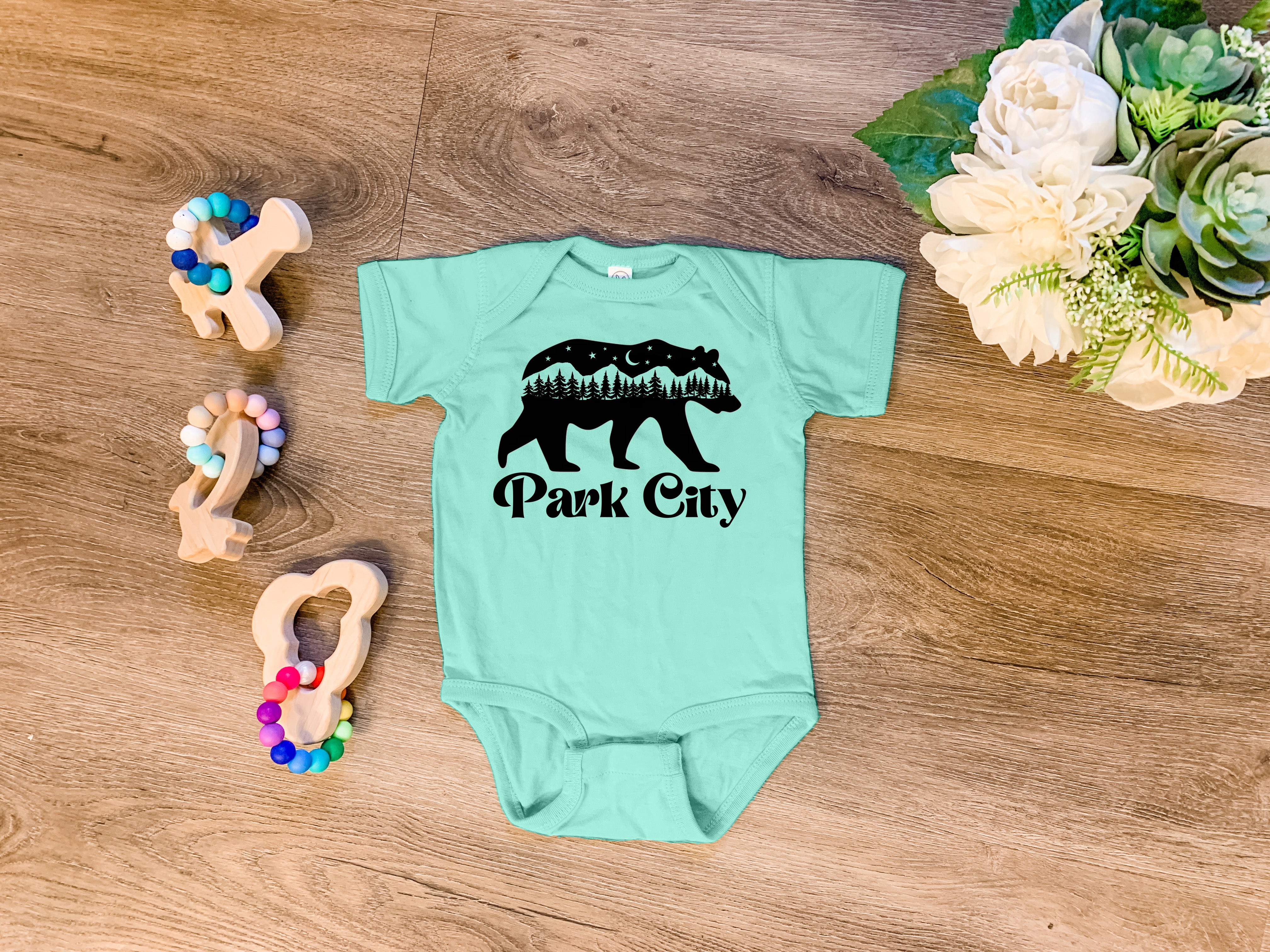 a baby bodysuit with a bear and trees on it