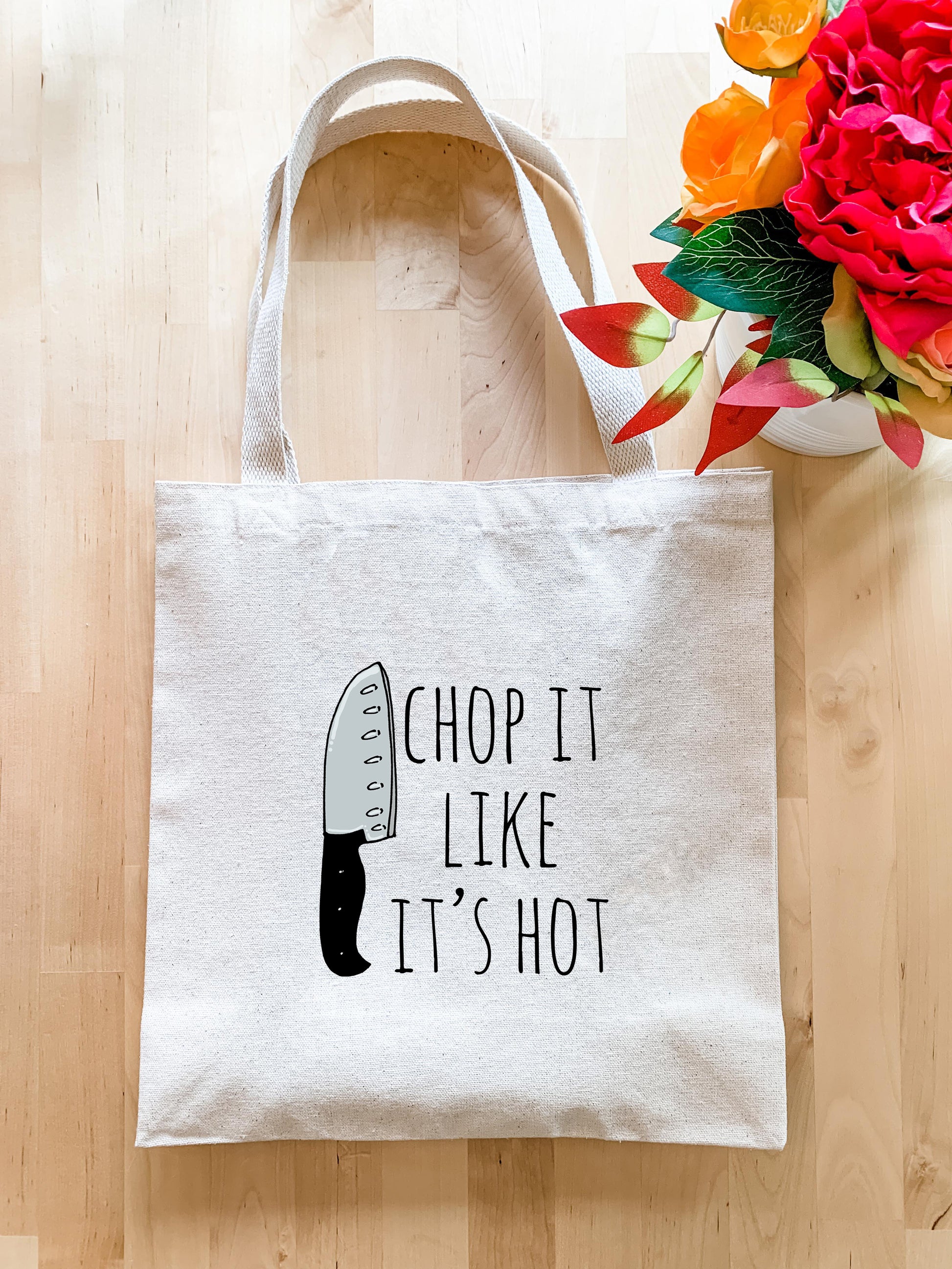 a tote bag with a knife on it next to a vase of flowers