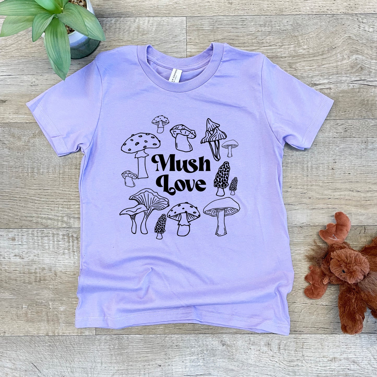 a purple t - shirt with mushrooms on it next to a teddy bear