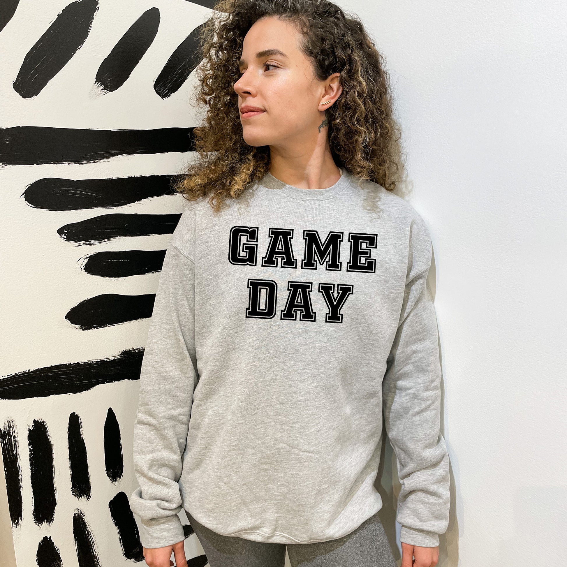 a woman standing in front of a wall with a game day sweatshirt on