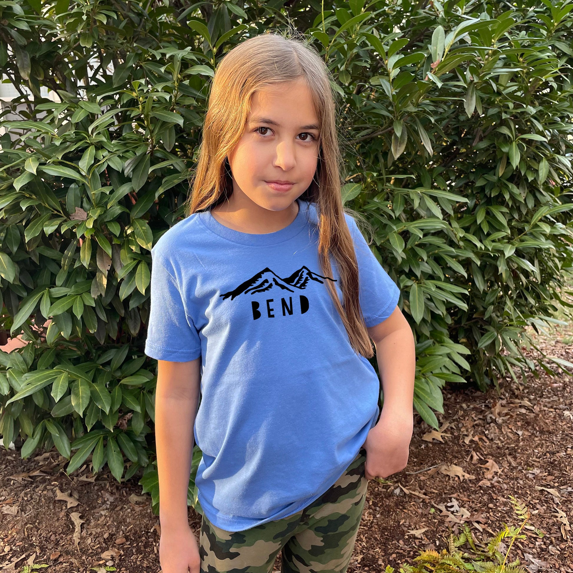 a young girl standing in front of a bush