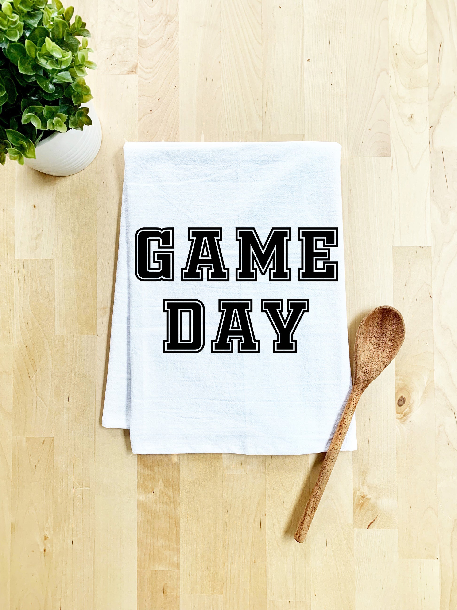 a dish towel that says game day next to a wooden spoon